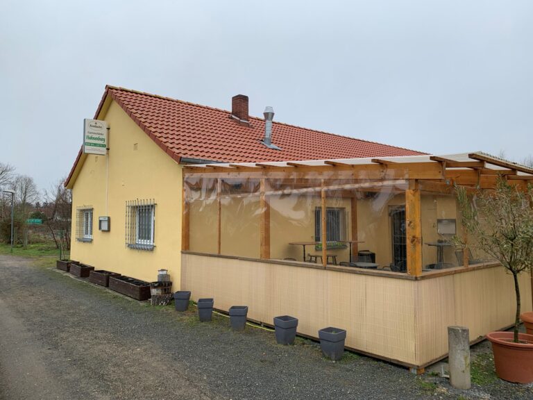 Das gelbe Vereinsheim mit hölzerner Terrasse und Windschutz